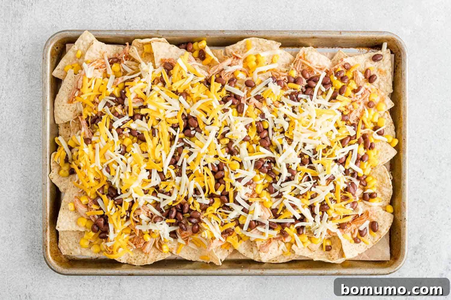 Backyard BBQ Chicken Nachos 12 The final layer of shredded cheese generously applied over all the nacho toppings before baking.