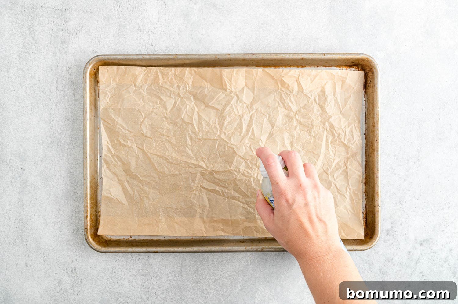 Backyard BBQ Chicken Nachos 5 A sheet of parchment paper being sprayed with nonstick cooking spray on a baking sheet, preparing it for nachos.