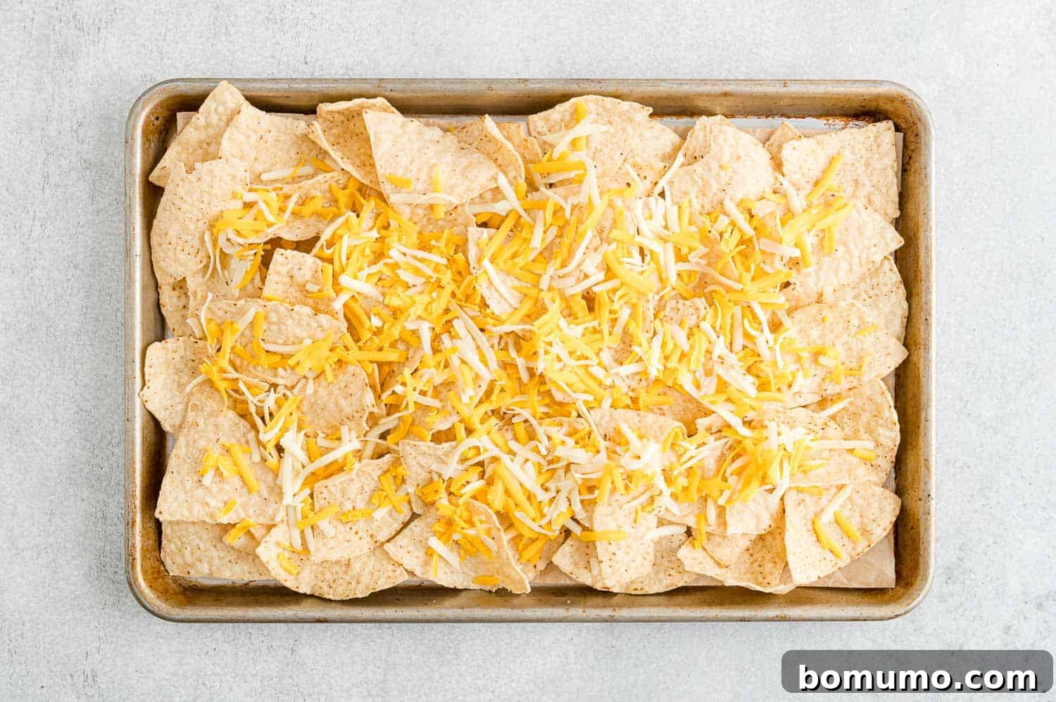 Backyard BBQ Chicken Nachos 7 Tortilla chips on a sheet pan, now covered with a generous layer of shredded cheese.