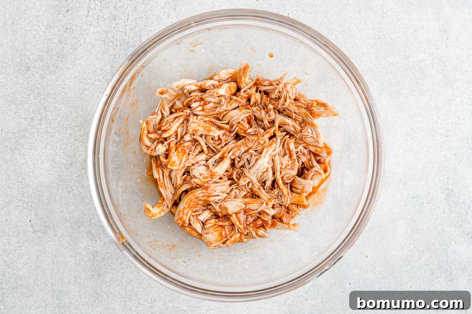 Backyard BBQ Chicken Nachos 8 Shredded chicken being mixed with BBQ sauce in a bowl, showing a rich, coated texture.