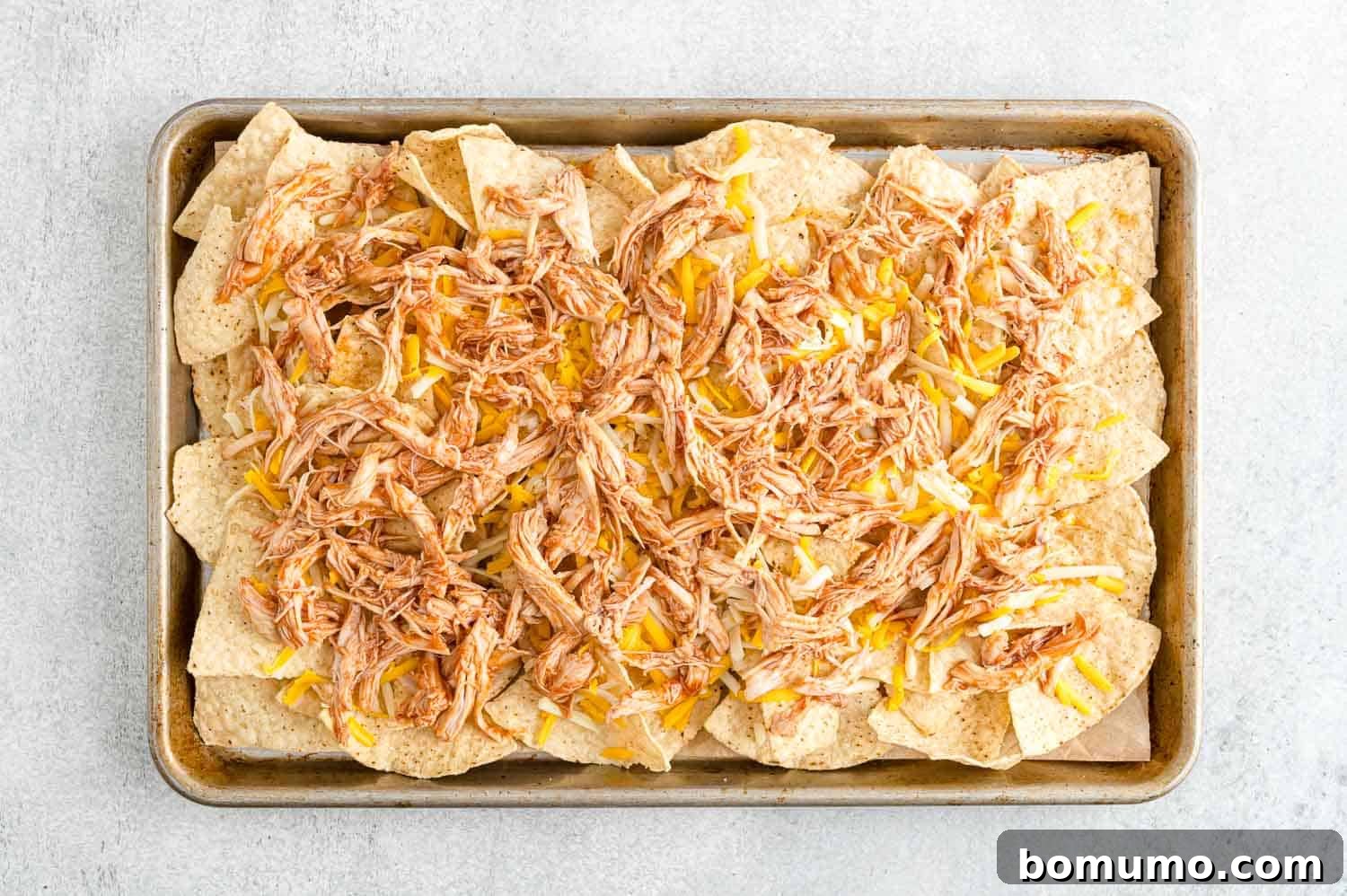 Backyard BBQ Chicken Nachos 9 The BBQ chicken mixture spread evenly over the cheesy tortilla chips on the baking sheet.