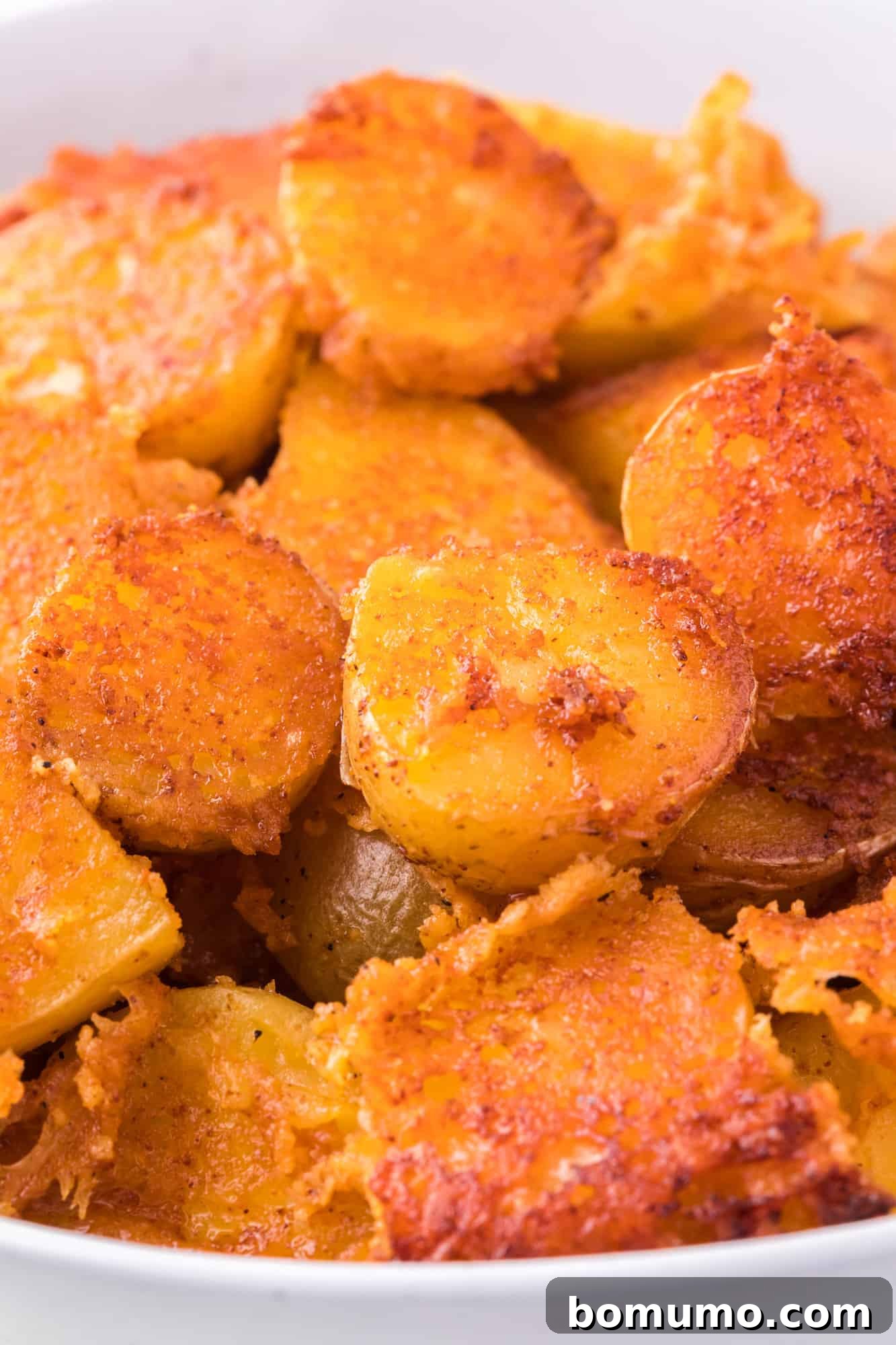 Close up of crispy parmesan potatoes in a white bowl, showcasing their golden crust.