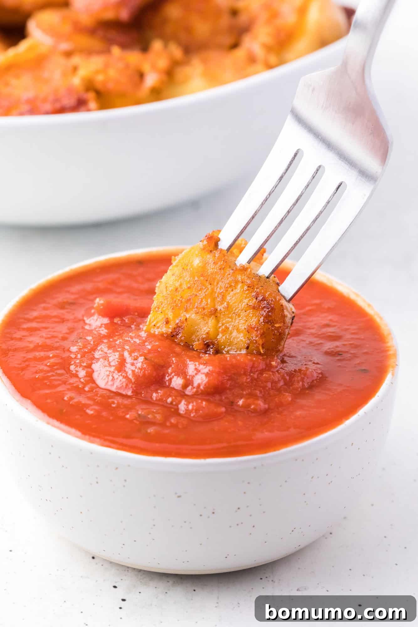 A fork dipping a crispy parmesan potato into a small bowl of marinara sauce.