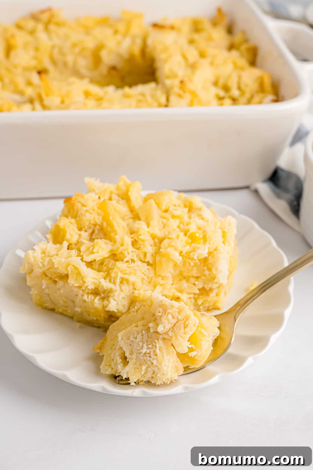 A forkful resting next to a generous serving of pineapple stuffing on a white plate, with a full casserole dish in the blurred background, highlighting its delicious texture.