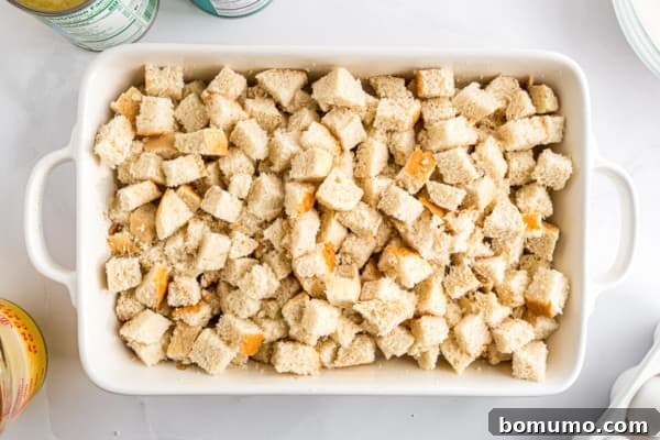 Uniformly cut bread cubes are gently added to a generously buttered casserole dish, forming the base layer for the pineapple stuffing.