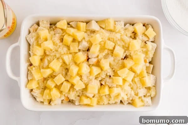 An overhead view captures the harmonious layering of pineapple stuffing ingredients within a large casserole dish, showcasing the bread base topped with pineapple.