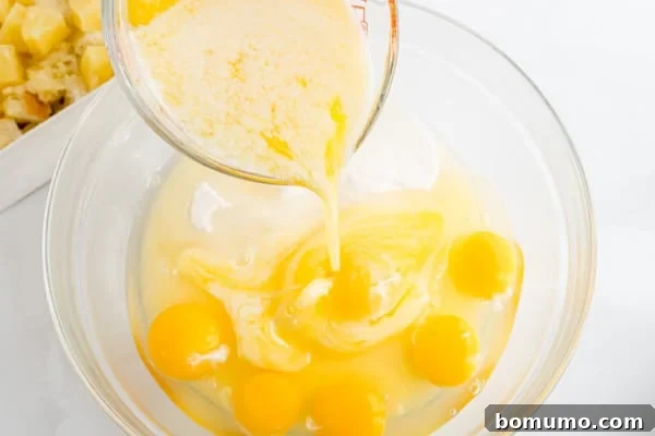A stream of melted butter and sugar mixture is carefully poured into a bowl of whisked eggs, preparing the rich custard base for the pineapple stuffing.