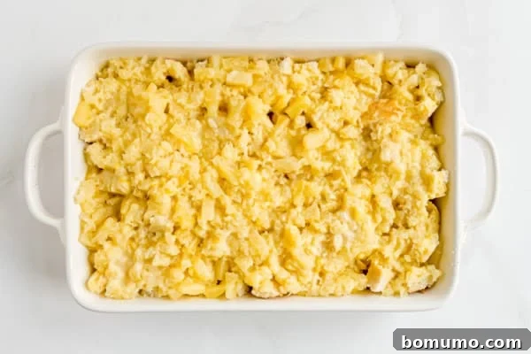 An overhead shot revealing the fully assembled pineapple stuffing in a large casserole dish, with the rich egg and butter mixture soaking into the bread and pineapple layers before baking.