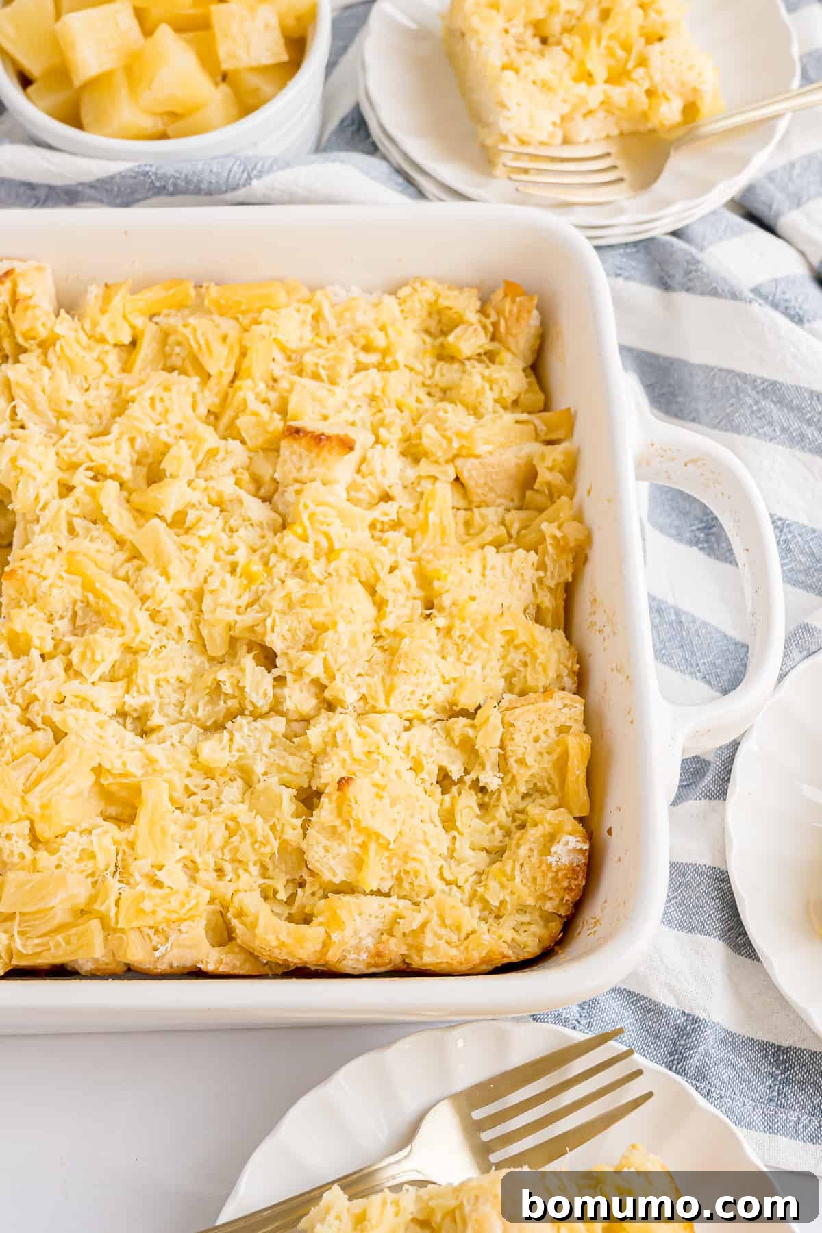 A warm, golden-brown pineapple stuffing casserole dish sits alongside individual servings on white plates, showcasing its appeal as a comforting holiday dish.
