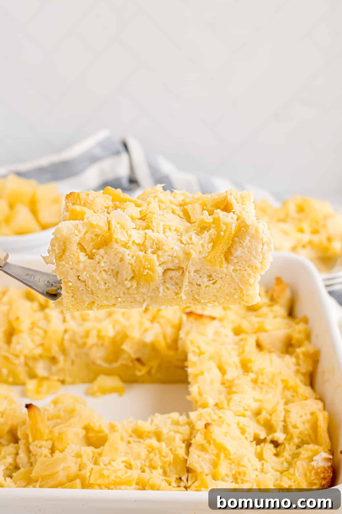 A perfect slice of golden-brown pineapple stuffing is carefully lifted from a baking dish with a spatula, showcasing its moist texture and inviting layers.