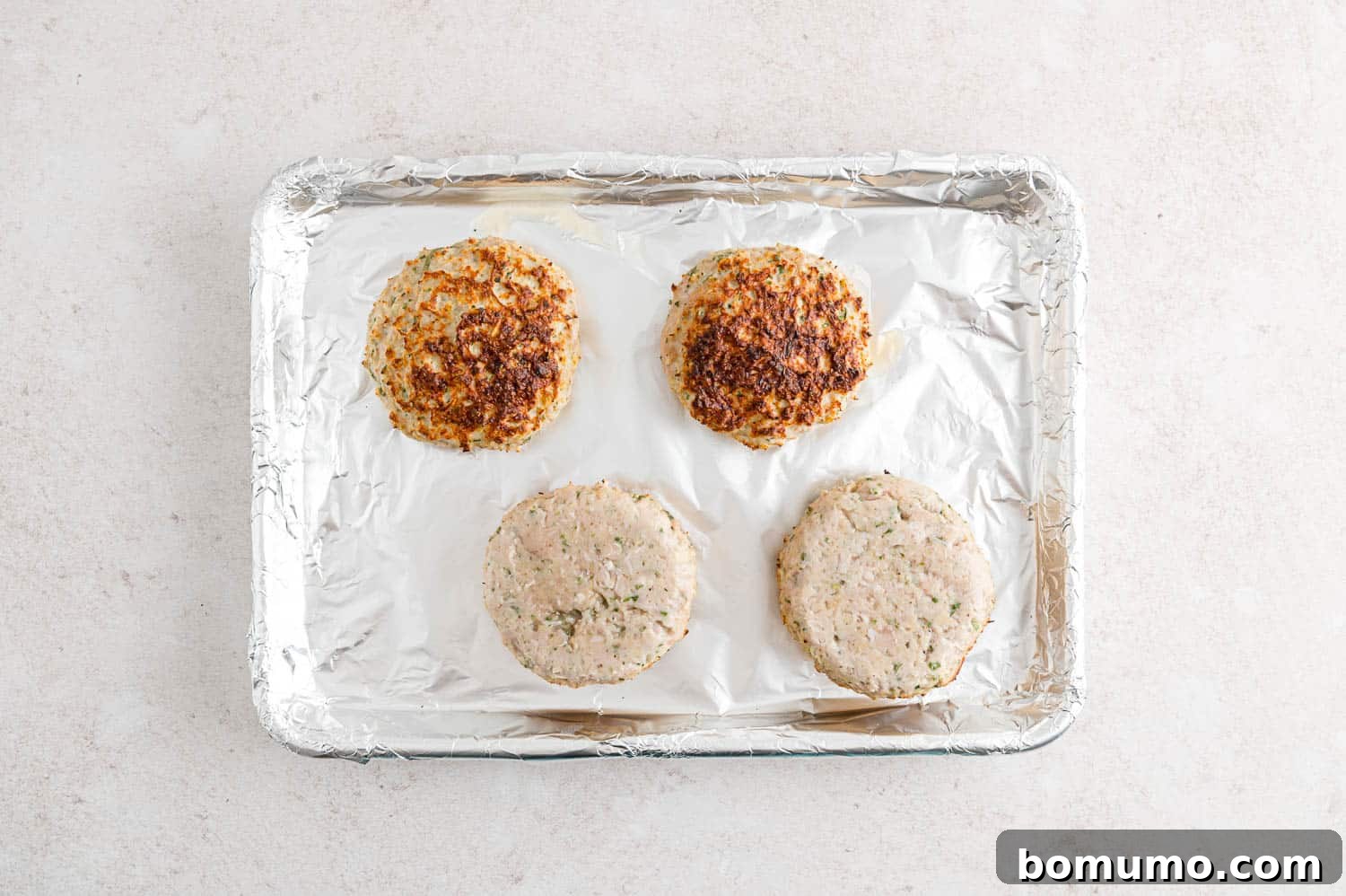 Two turkey burgers, halfway through the broiling process, showing a golden-brown sear on one side.