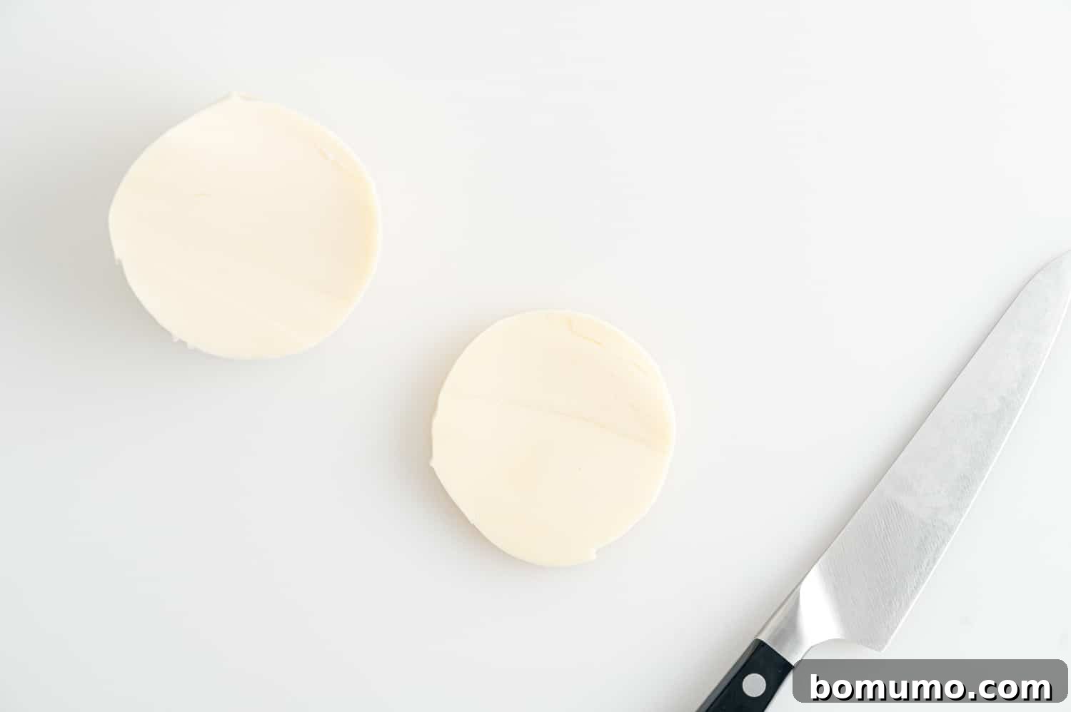 A close-up of a log of fresh mozzarella cheese being precisely sliced, preparing it for the burgers.
