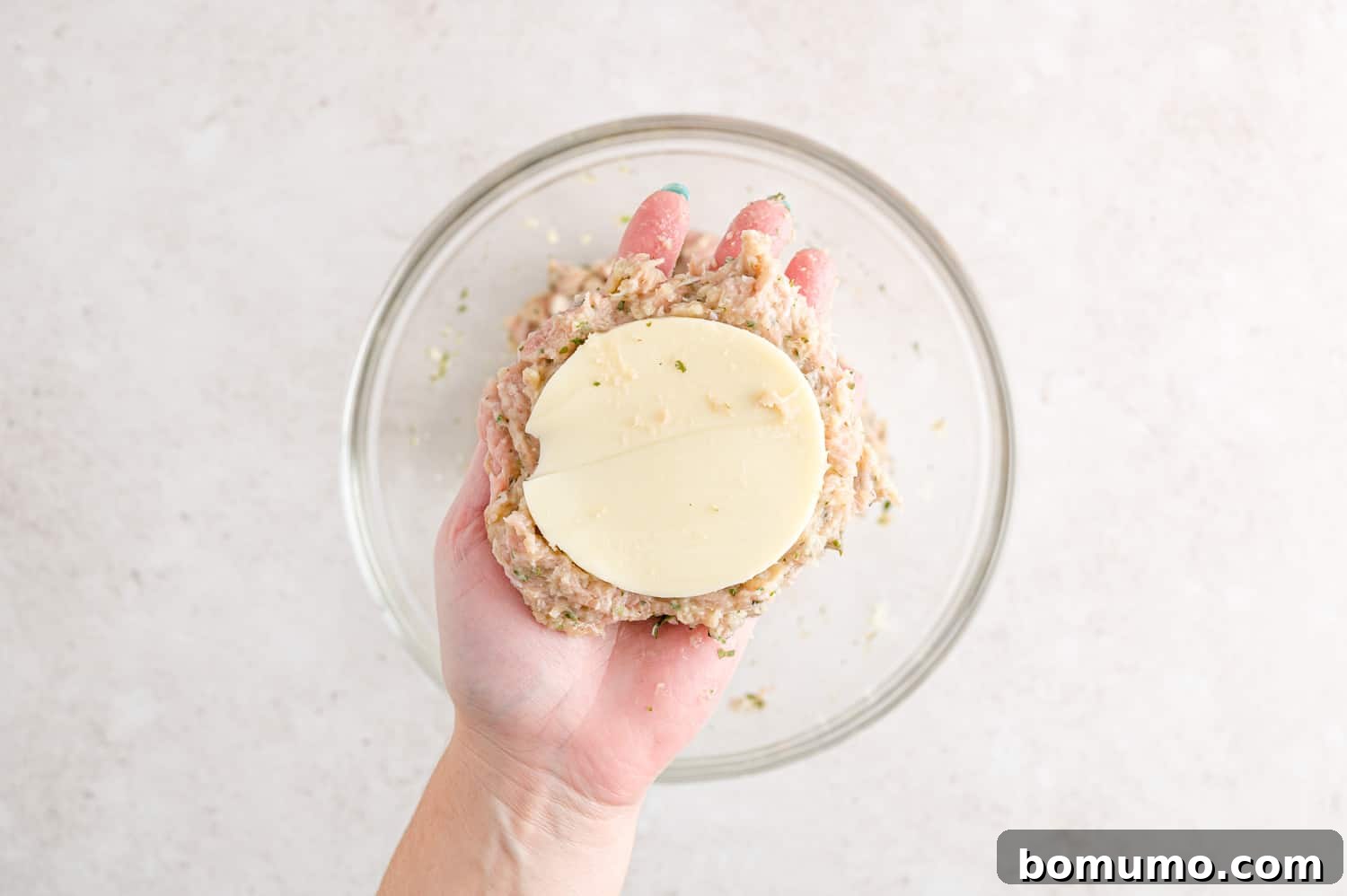 A turkey burger patty being carefully formed around a slice of mozzarella cheese.