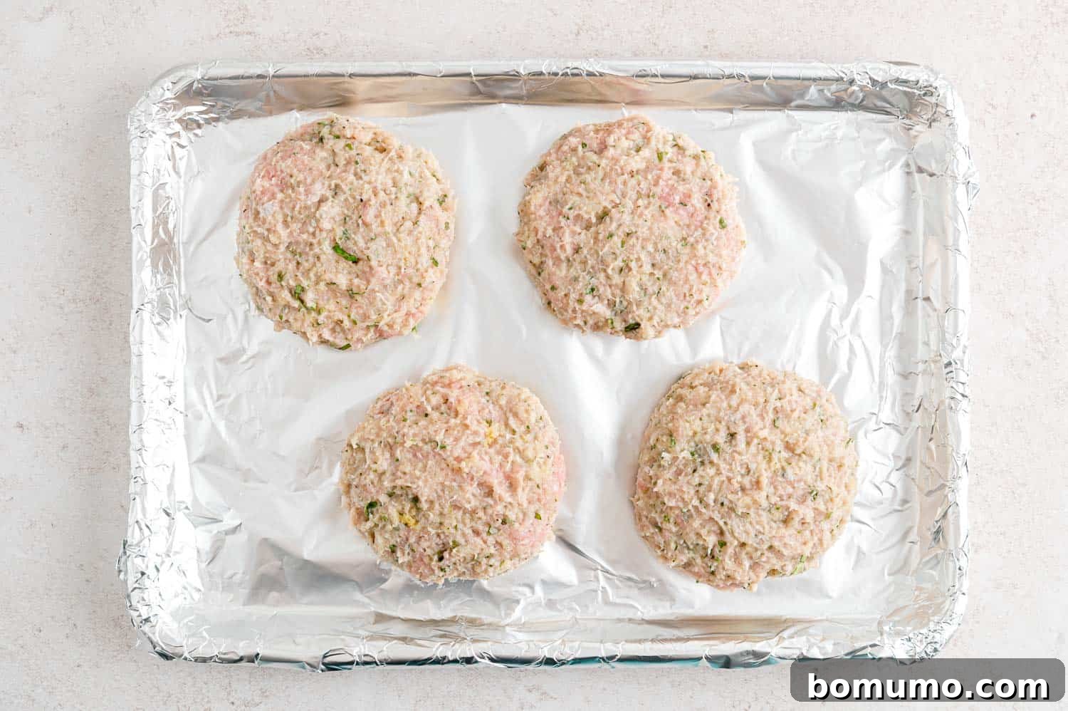 Four perfectly shaped, uncooked turkey burgers, ready for broiling.
