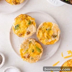 Three egg white muffins with melted cheese and visible broccoli pieces are arranged on a white plate, surrounded by ingredients and kitchen items on a light countertop, highlighting their delicious appearance.