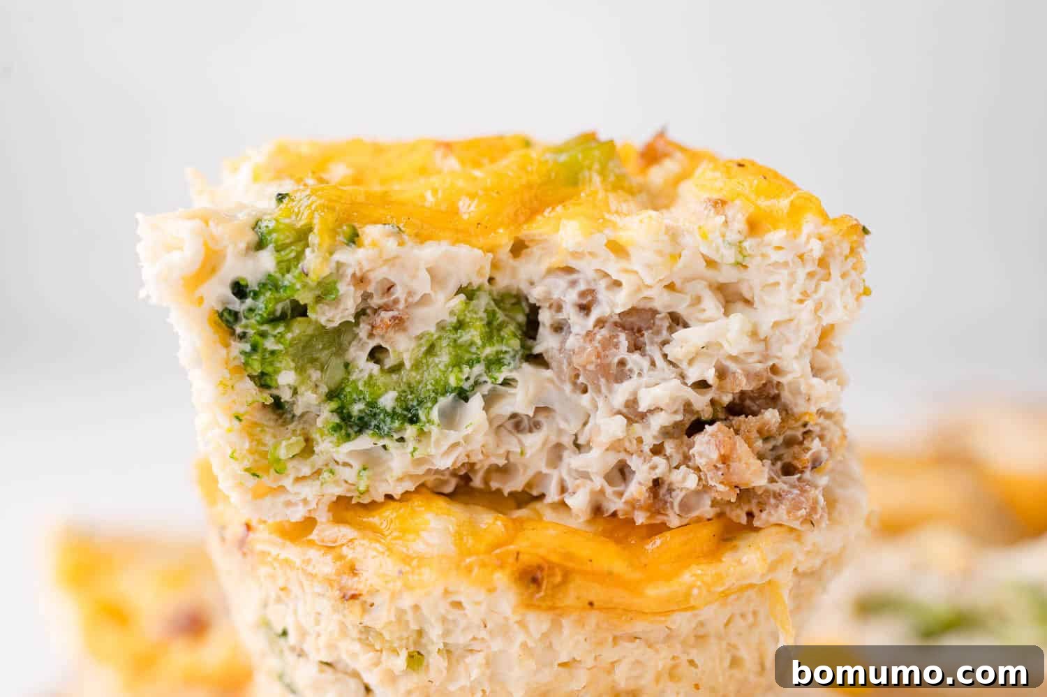 Protein-Packed Egg White Bites 3 A close-up of a perfectly baked egg muffin with visible broccoli florets, savory sausage crumbles, and melted cheddar cheese, showcasing its moist texture and delicious layers.