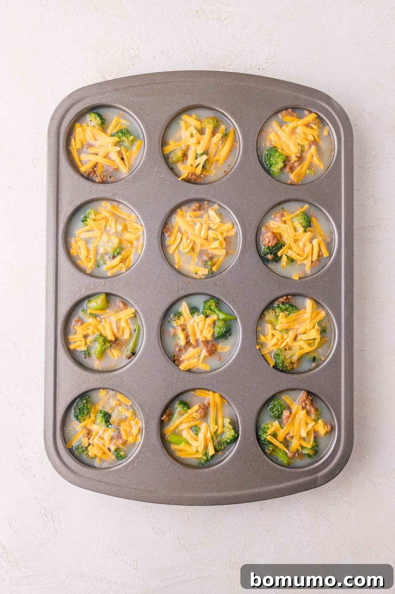 Protein-Packed Egg White Bites 9 A muffin tin filled with the unbaked egg mixture, chopped broccoli, sausage, and shredded cheese, showing the complete assembly before baking.