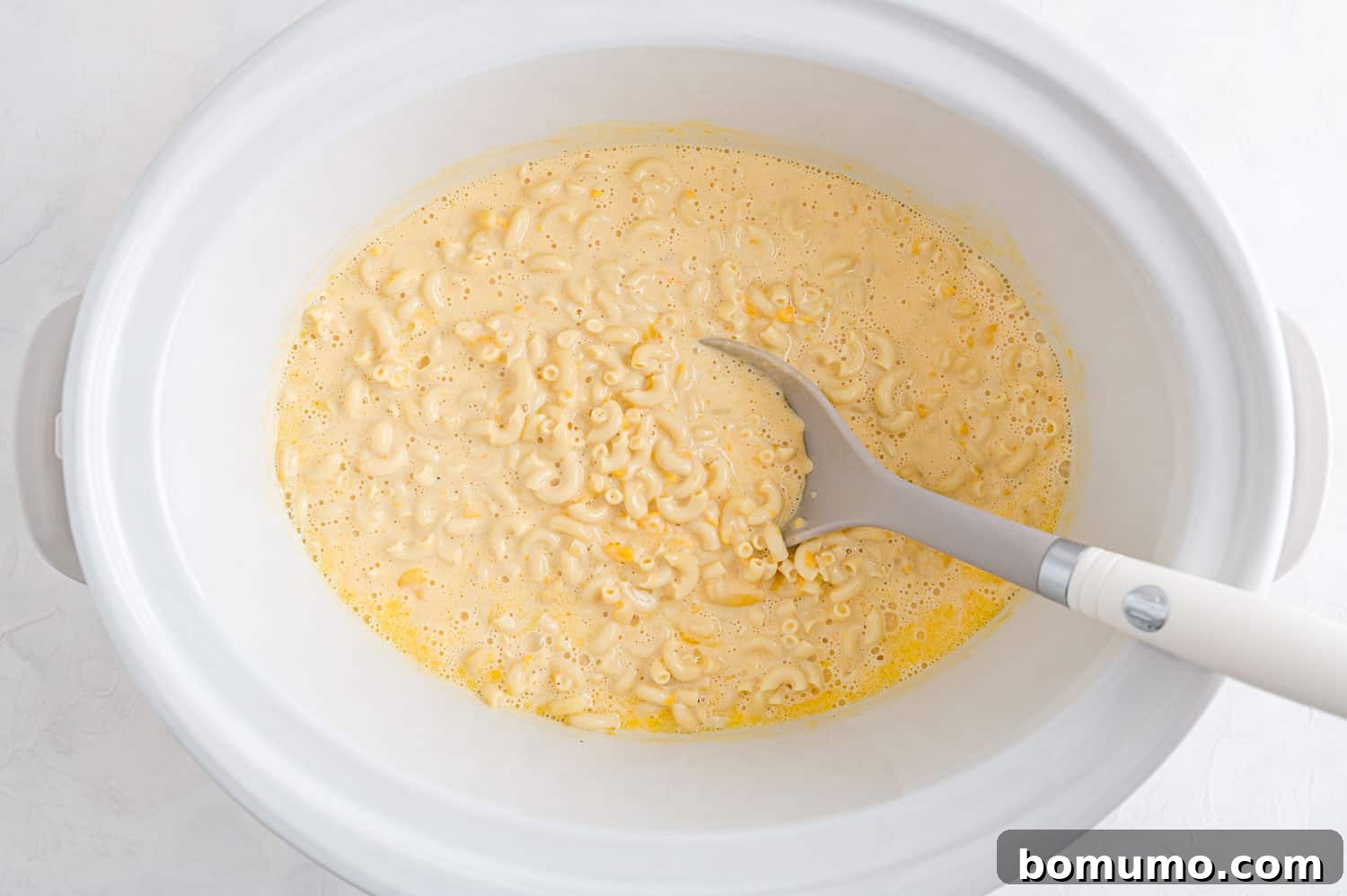 Creamy mac and cheese being stirred for the second time in the slow cooker, showing its increasing richness and perfectly cooked pasta strands.