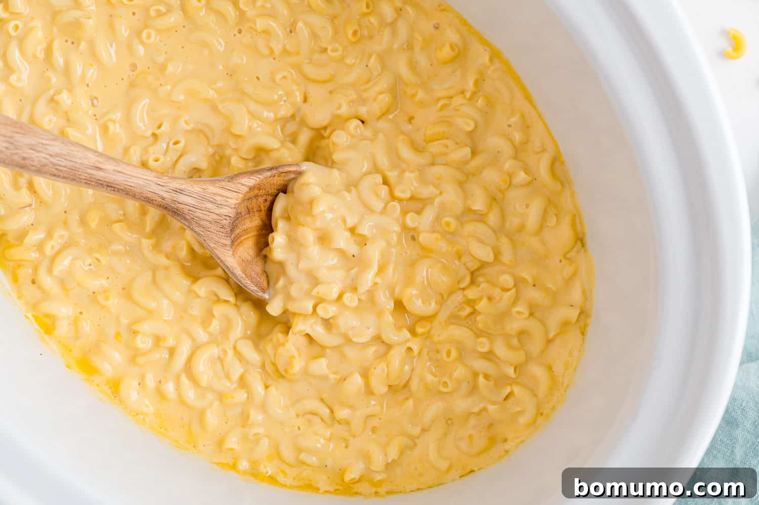 Rich, creamy macaroni and cheese being stirred one final time in the slow cooker, showcasing its perfectly smooth and thick texture, ready for serving.