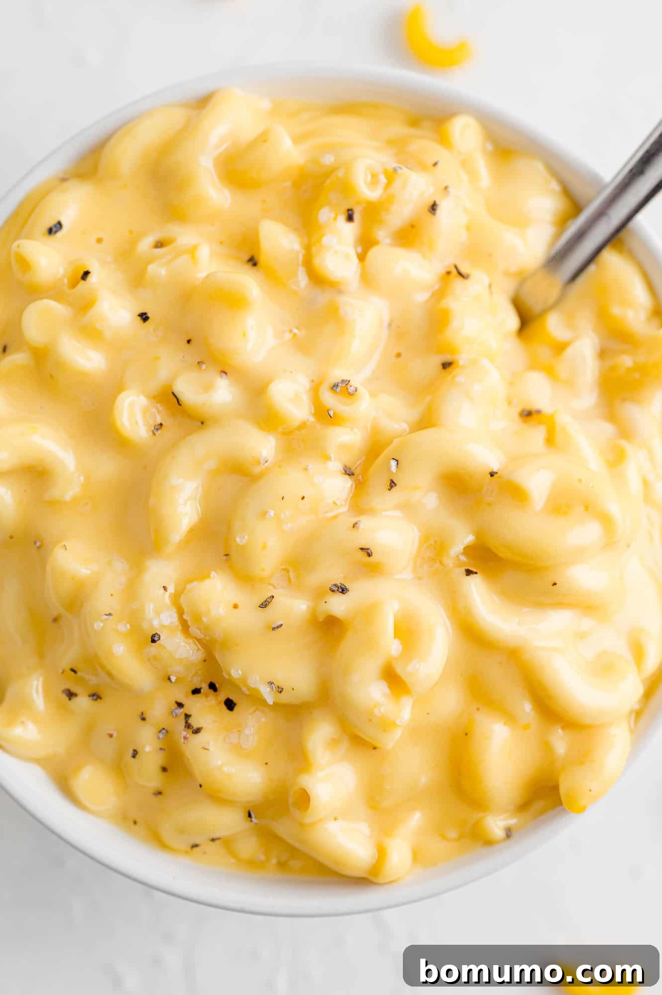 A serving spoon gracefully lifts a generous portion of creamy macaroni and cheese from a slow cooker, illustrating its delightful texture and readiness to be dished out.