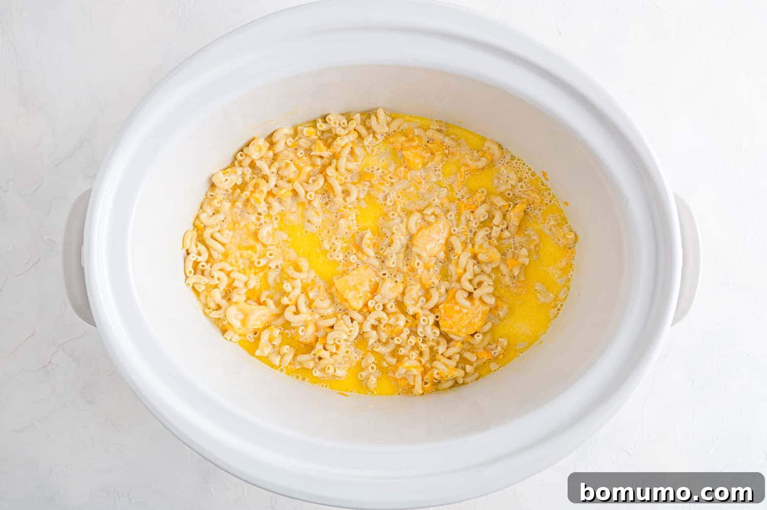 The crockpot mac and cheese after one hour of cooking, showing the cheese beginning to melt into the sauce and the pasta starting to soften in the liquid.