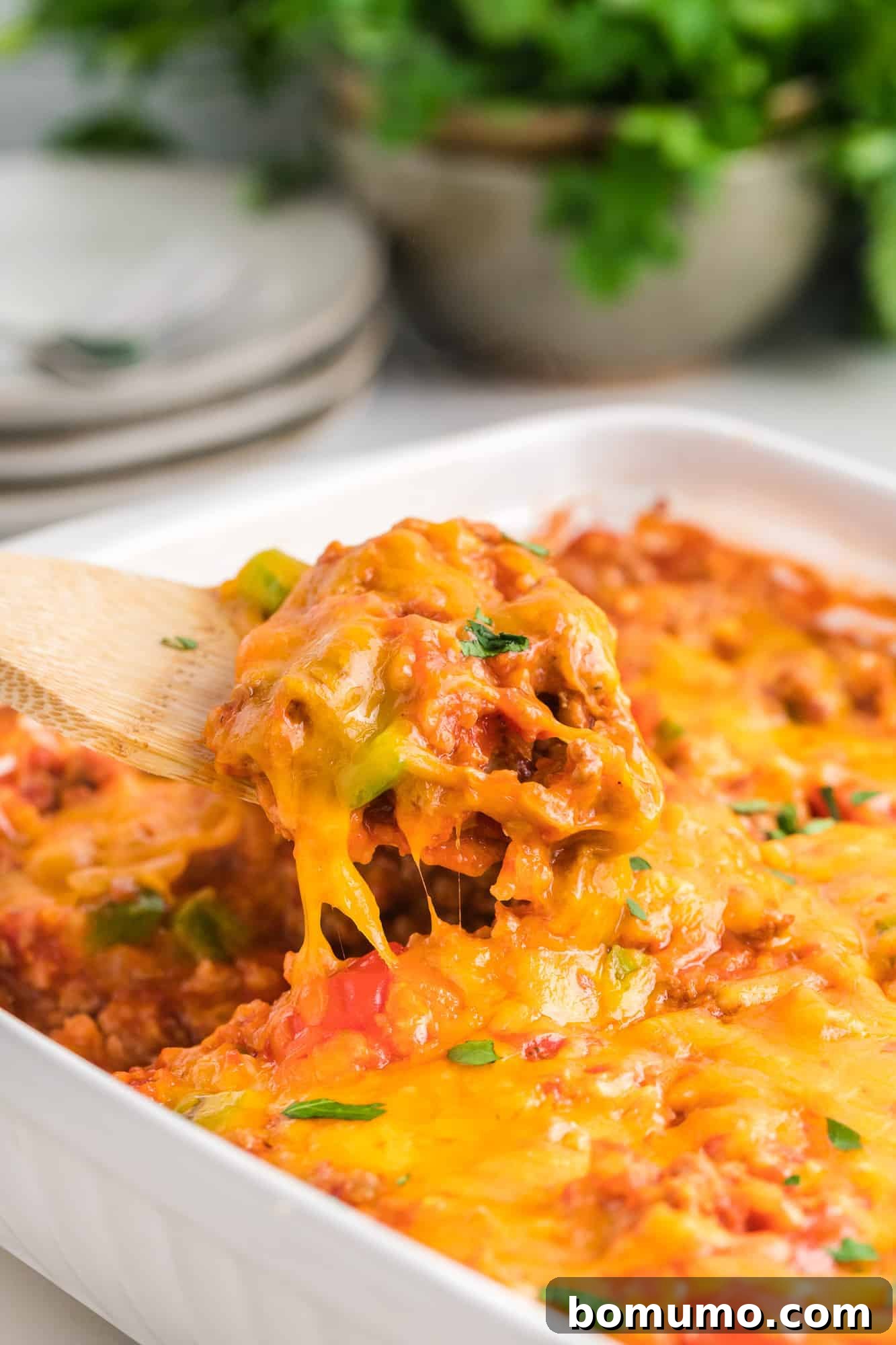 Healthy Stuffed Pepper Casserole being scooped out of a white casserole dish, featuring ground turkey, brown rice, and melted cheddar cheese.