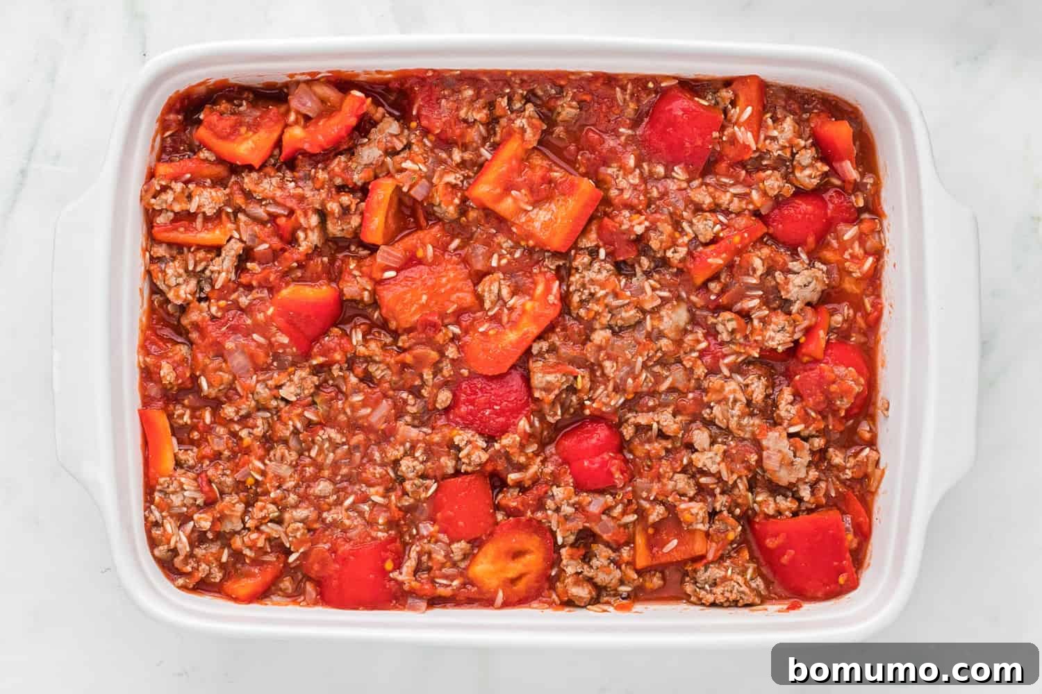 Stuffed pepper casserole mixture tightly covered with aluminum foil in a baking dish, prepared for baking.