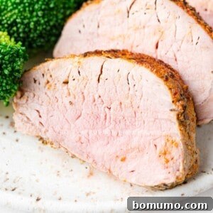 Sliced air fryer pork tenderloin, with vibrant green broccoli visible in the corner of the photo.