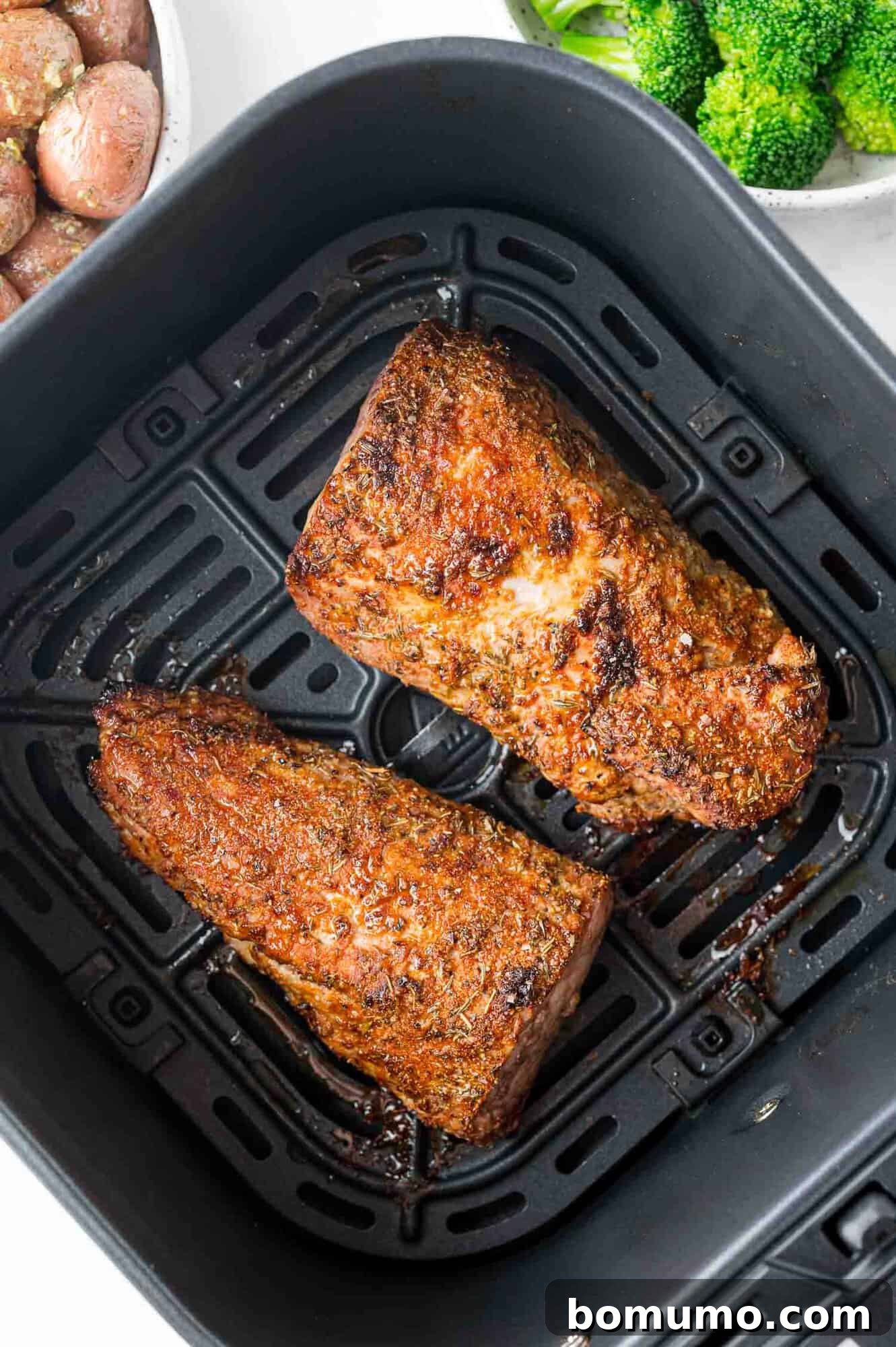 Raw pork tenderloin, expertly cut into two manageable pieces, placed in an air fryer basket, ready for cooking.