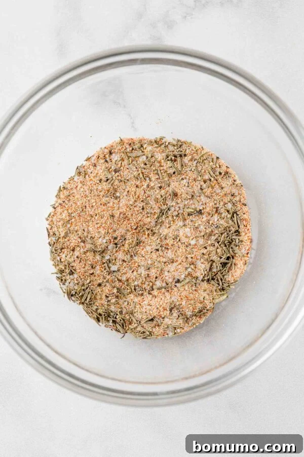 A vibrant blend of spices and herbs, forming a perfectly mixed rub, contained within a clear glass bowl.