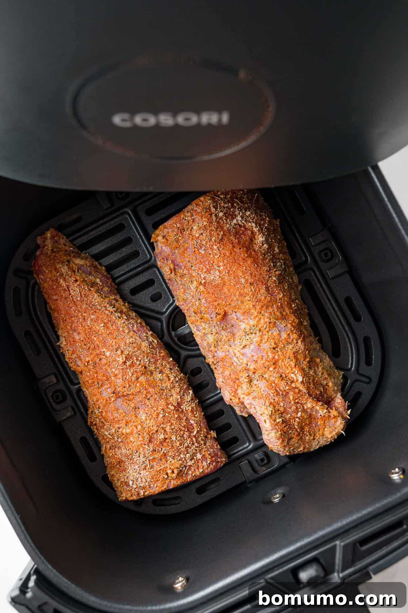 Uncooked, seasoned pork tenderloin nestled in the basket of an air fryer, ready to be cooked.