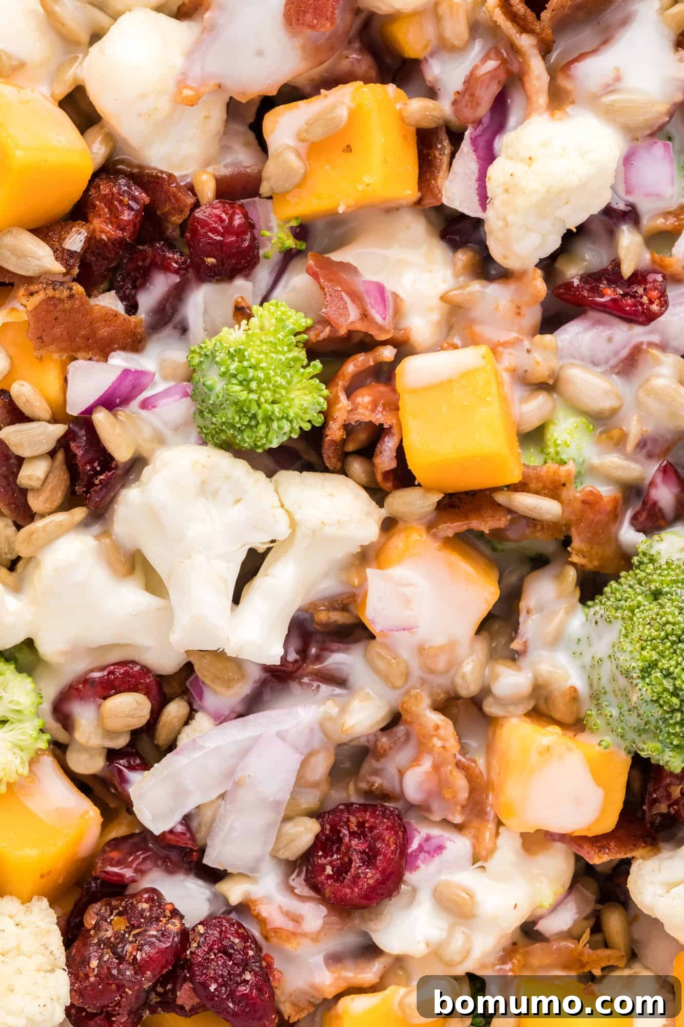Close up view of the textured, creamy broccoli cauliflower salad, showing florets, bacon, and cranberries.