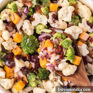Overhead view of broccoli cauliflower salad in a white bowl with a wooden spoon.