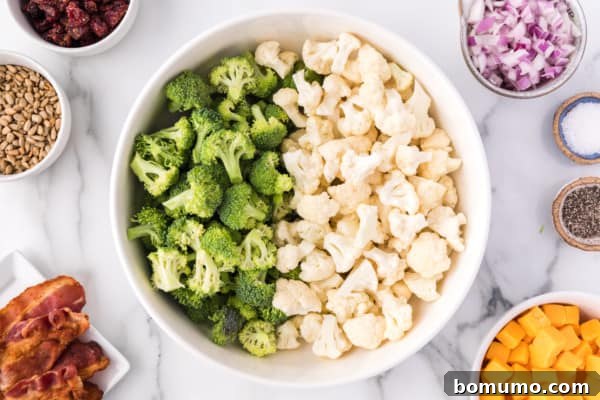 Broccoli and cauliflower florets in a bowl surrounded by salad ingredients, illustrating the prep phase.