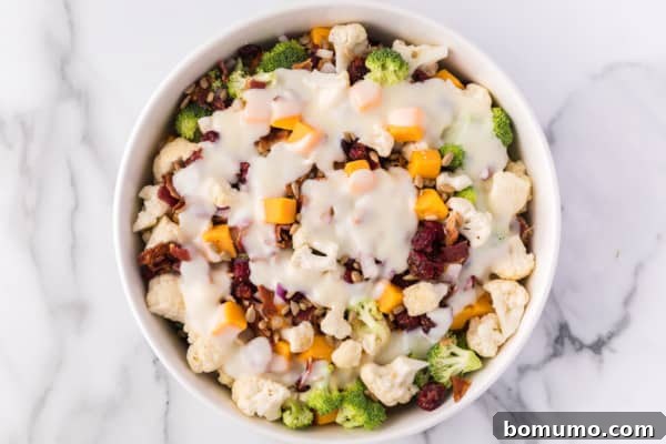 Dressing being drizzled over a bowl of broccoli cauliflower salad ingredients, ready for tossing.