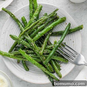 Roasted green beans on a round white plate.