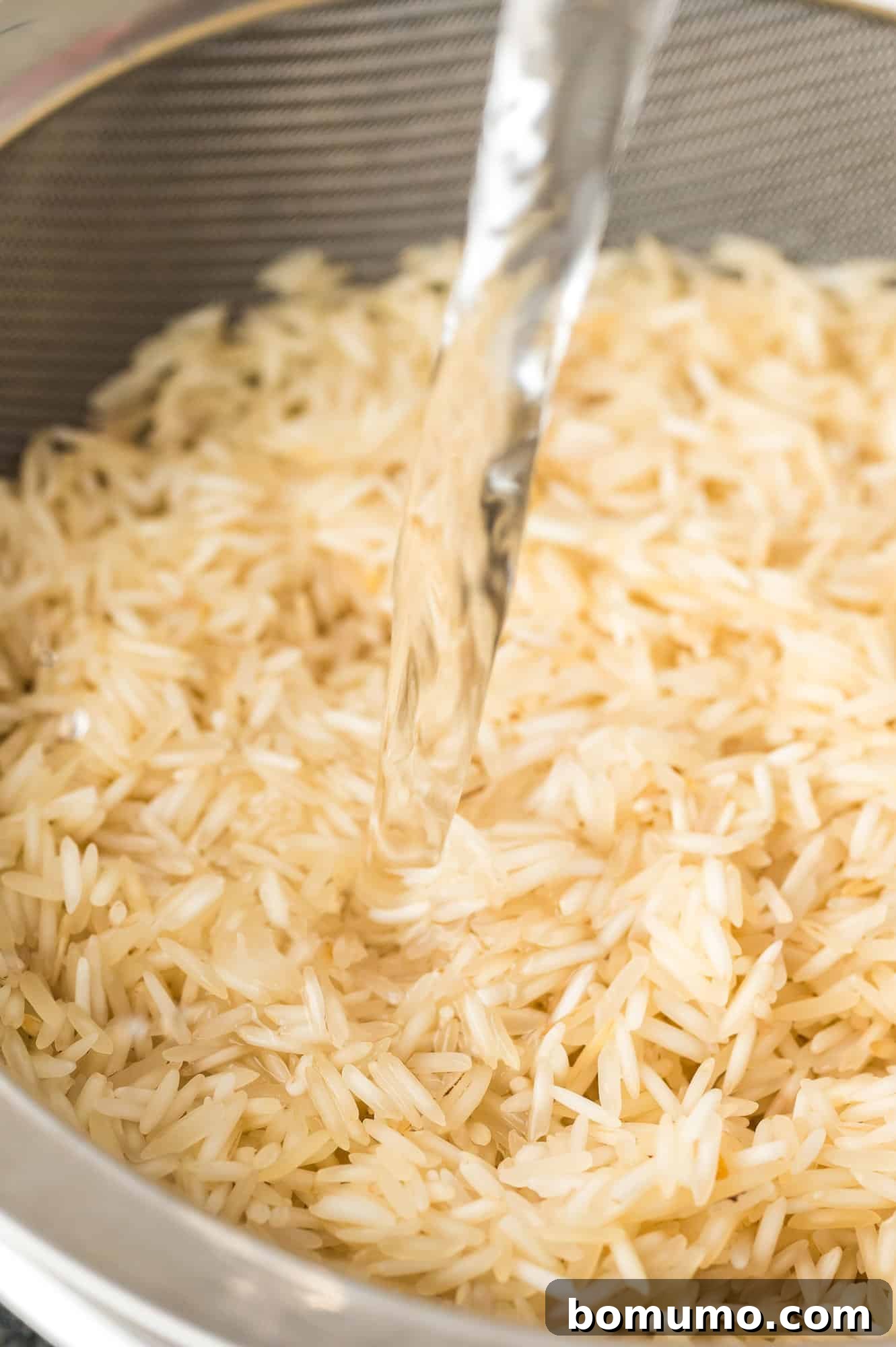 Basmati rice being rinsed under cold water in a fine mesh colander.