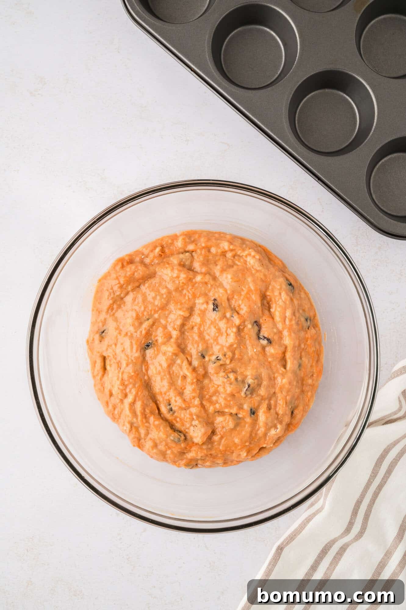 Completed muffin batter, in a clear glass mixing bowl, showcasing its readiness for baking.