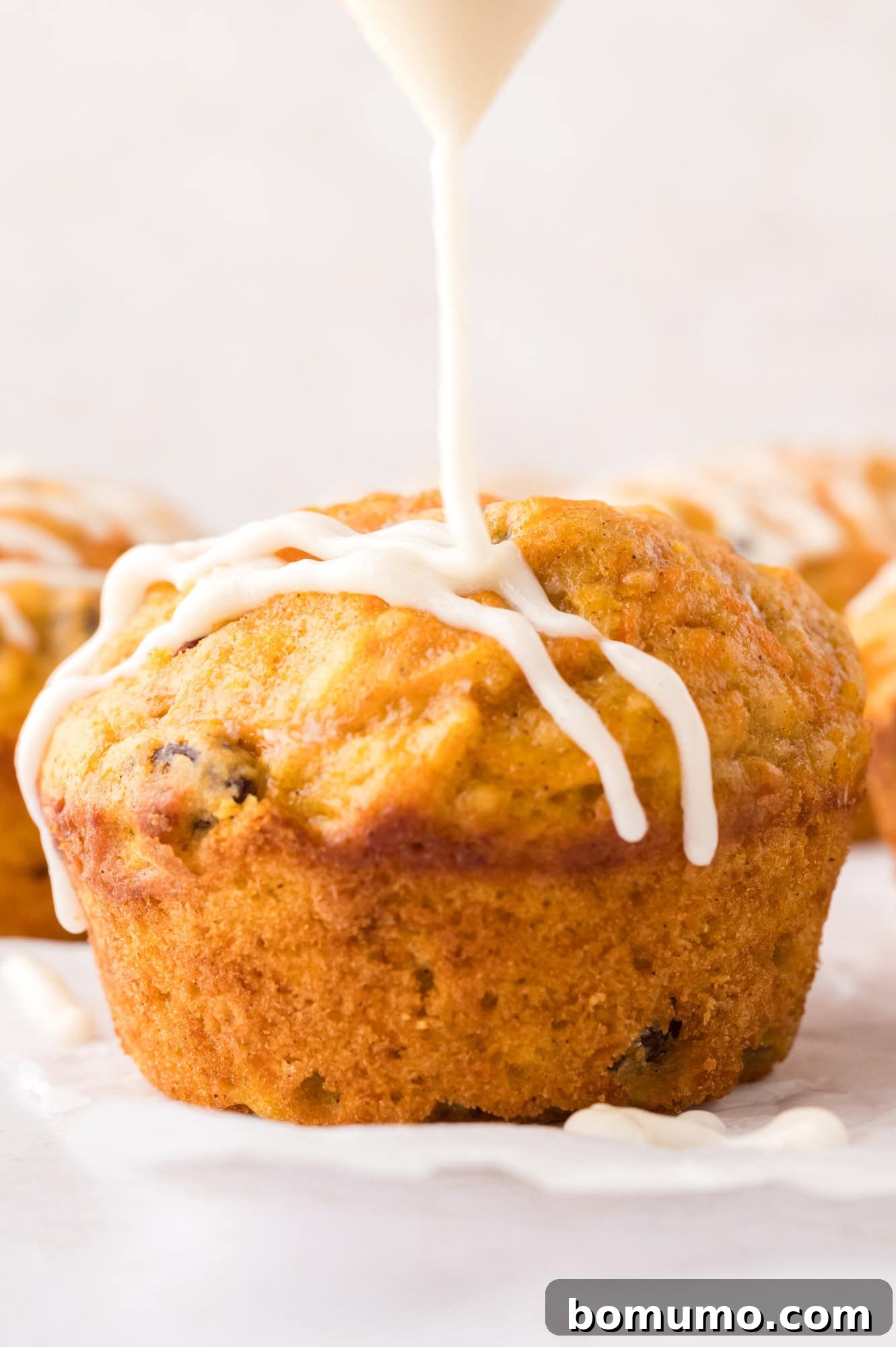 Cream cheese glaze being carefully drizzled over baked carrot cake muffins, enhancing their appeal.
