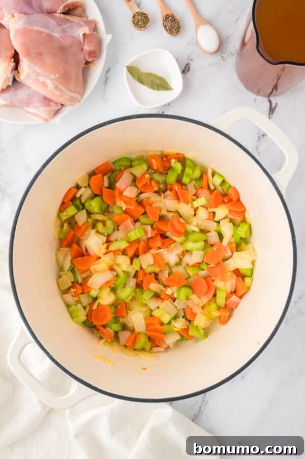 Diced onions, carrots, and celery sautéing in melted butter in a large pot, forming an aromatic base.