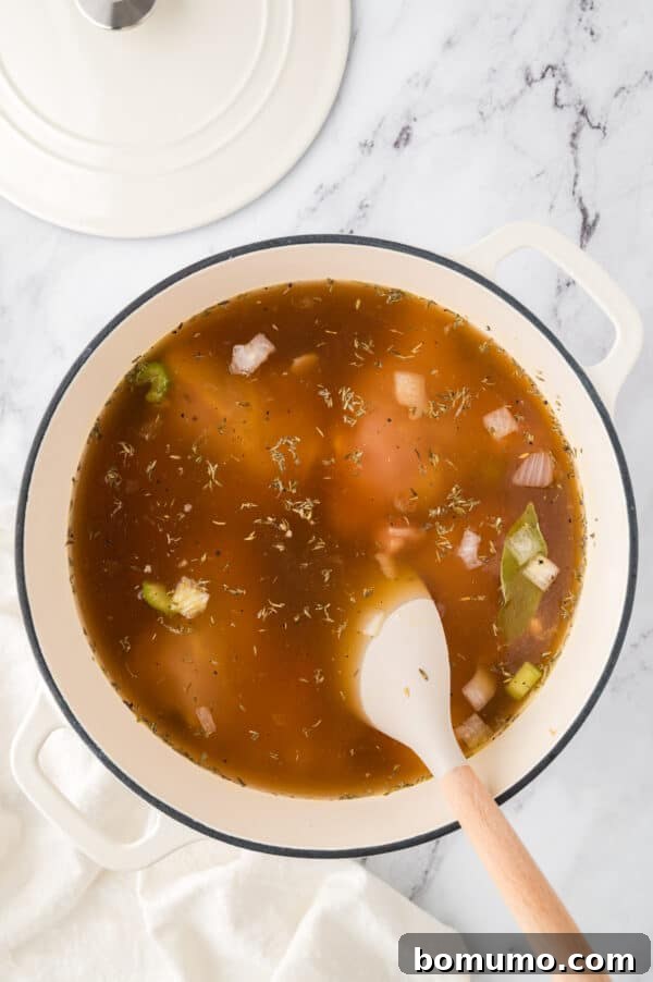 Chicken soup ingredients, including bone-in chicken thighs and broth, being gently stirred together in a large pot, ready for simmering.