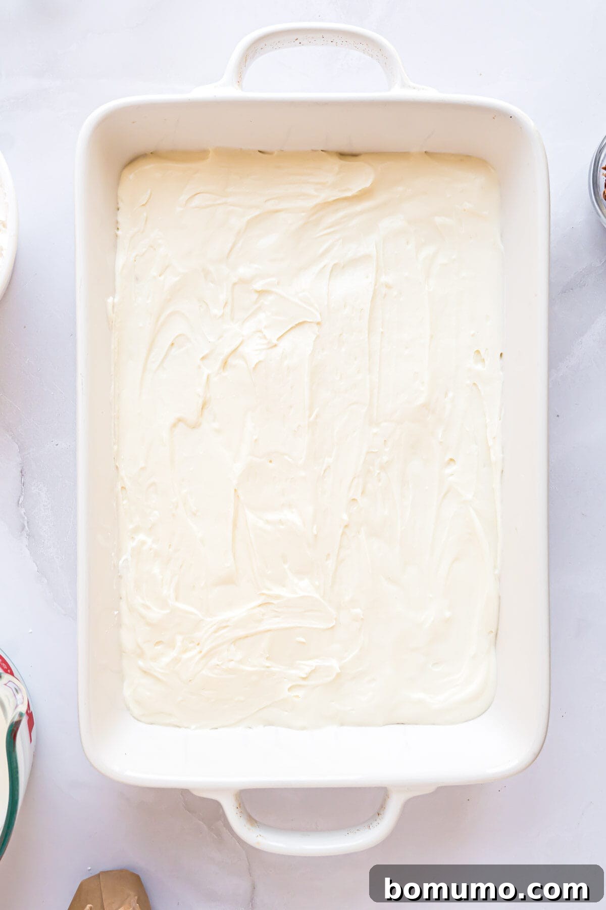 The smooth, creamy cream cheese layer spread evenly over the pecan crust in the baking dish.