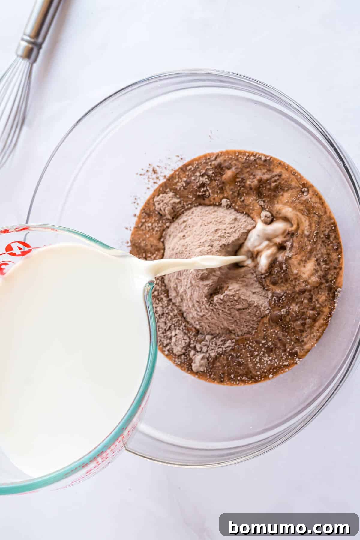 Instant chocolate pudding mix and cold milk being combined in a bowl with a whisk.