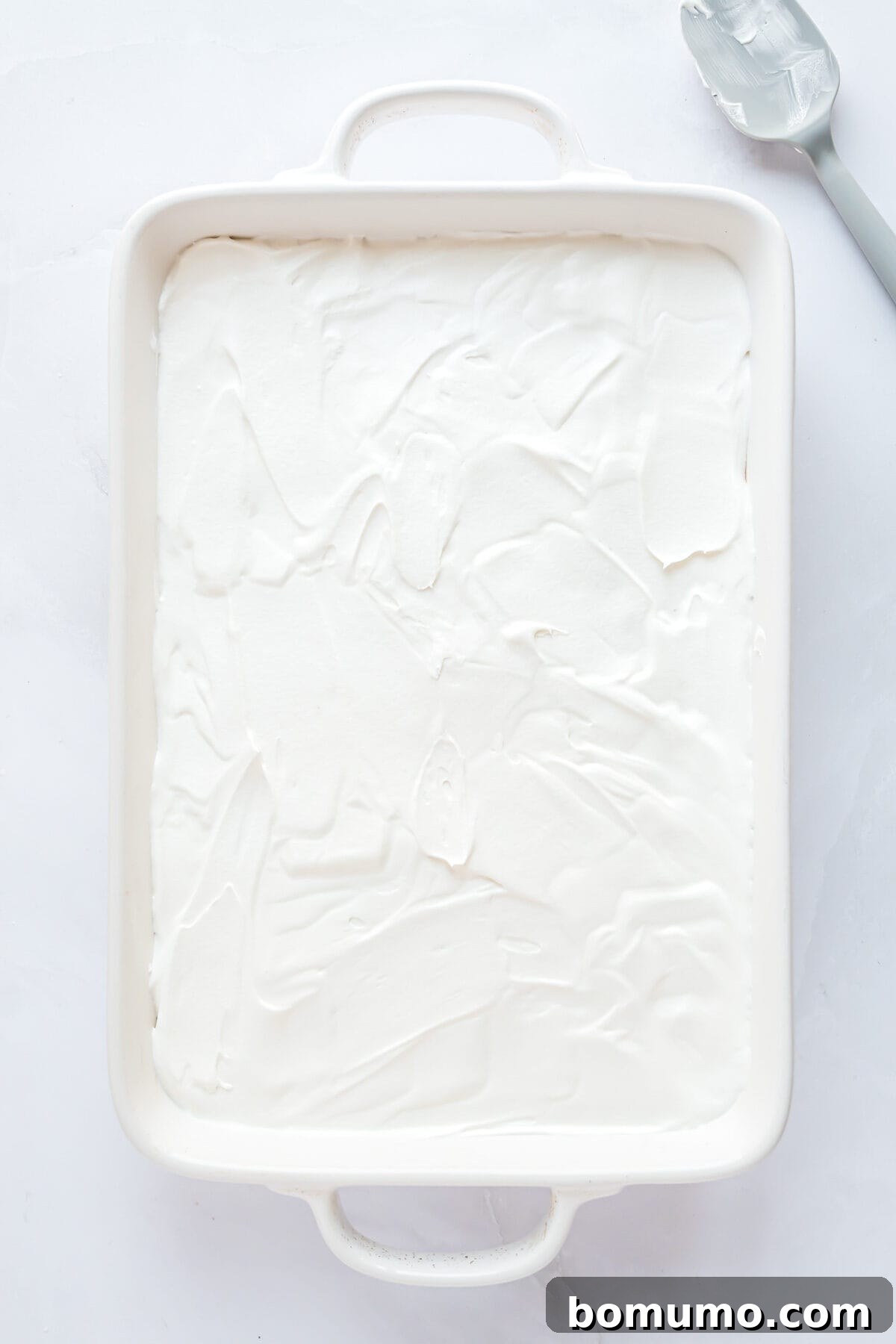 The final layer of fluffy whipped cream generously spread over the chocolate pudding in the Chocolate Delight dessert.