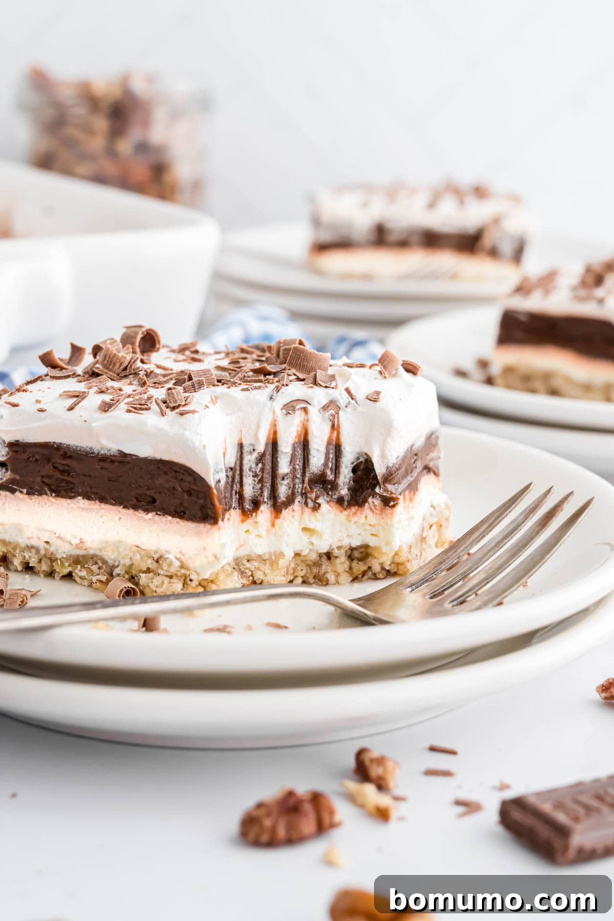 A close-up of a slice of Chocolate Delight dessert, with a bite removed, clearly showing the fork marks and the distinct layers of crust, cream cheese, pudding, and whipped topping.