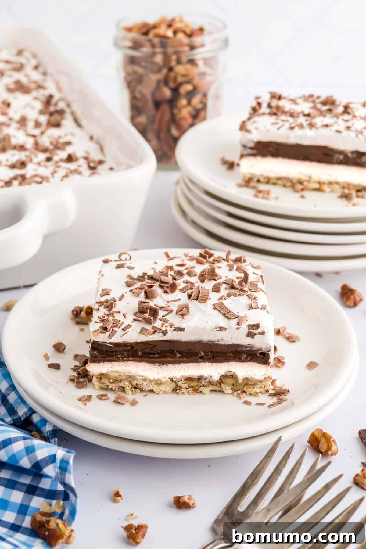 A pristine slice of Chocolate Delight resting on a white plate, with another tempting slice blurred in the background, showcasing the dessert's perfect layers.
