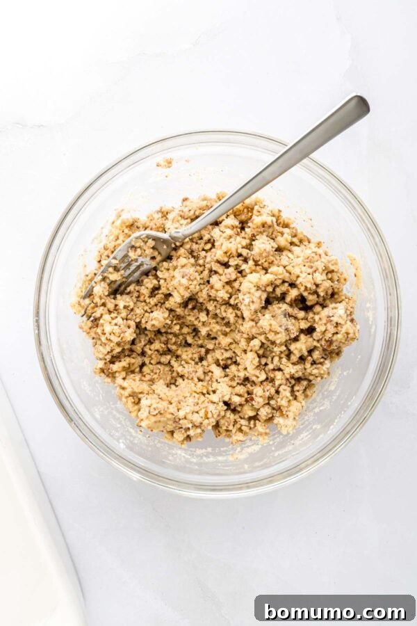 The pecan cookie crust ingredients, now mixed together in a clear glass bowl, showing a crumbly but cohesive texture.