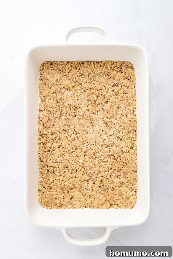 The pecan cookie crust firmly pressed into the bottom of a glass baking dish, forming an even layer.