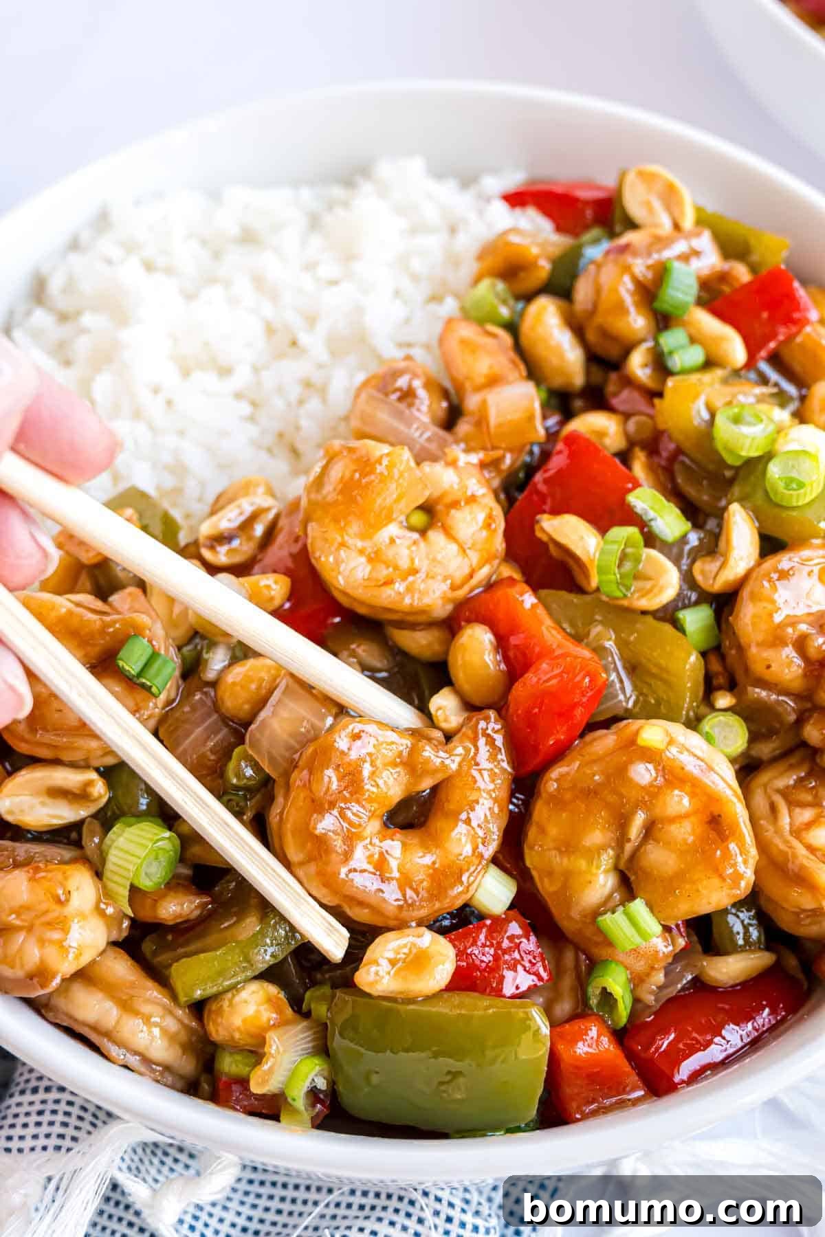 Fiery Peanut Shrimp Delight 12 A single piece of perfectly cooked Kung Pao shrimp held delicately between chopsticks, highlighting its succulence.