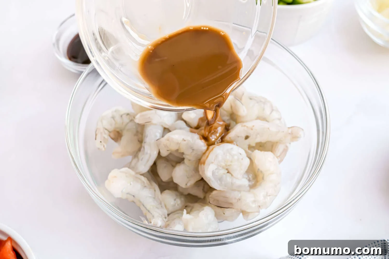 Fiery Peanut Shrimp Delight 5 The process of pouring marinade over raw, uncooked shrimp, ensuring even coating for optimal flavor.